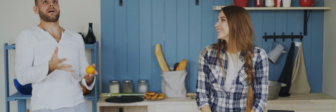 Attractive loving couple having fun in the kitchen. Handsome man juggle with fruits to impress his girlfriend at home