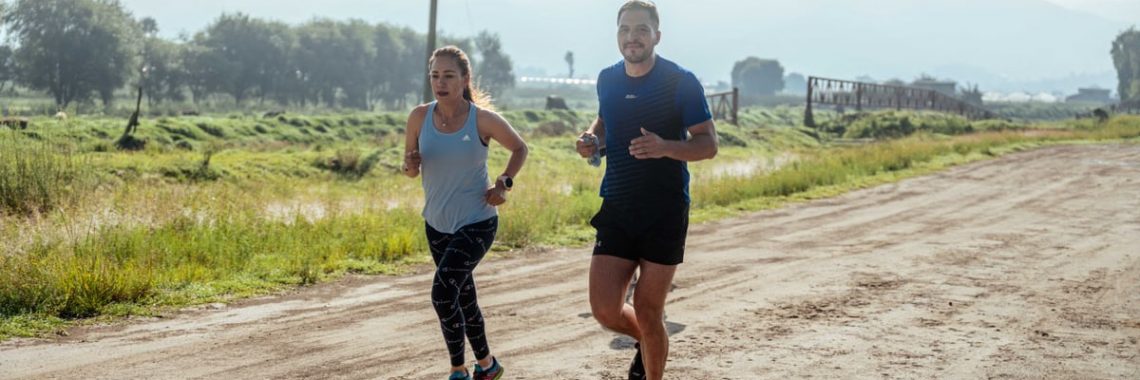 Active couple jogging on a dirt road in a scenic rural area under the bright sun.